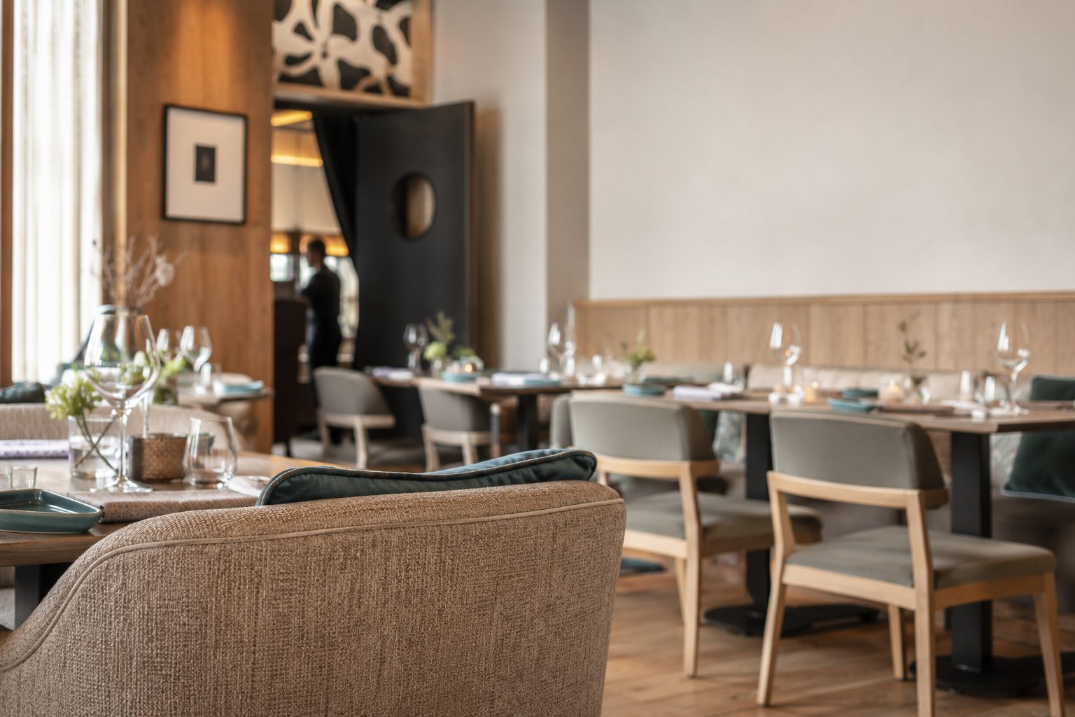 Salle de restaurant professionnelle : fauteuil en tissu bouclé, banquette, chaises tapissées et service en arrière-plan.